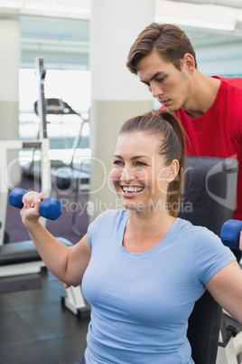 Personal trainer helping client lift dumbbells