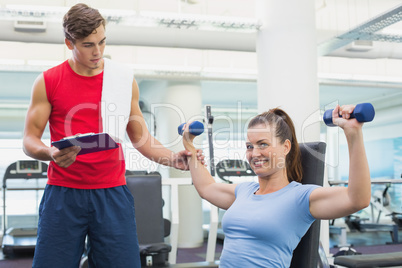 Personal trainer helping client lift dumbbells