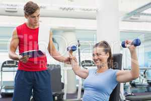 Personal trainer helping client lift dumbbells