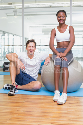 Personal trainer and client smiling at camera with exercise ball