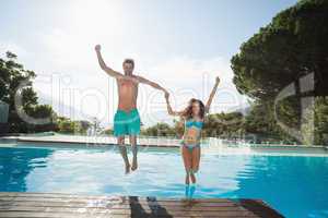 Cheerful young couple jumping into swimming pool