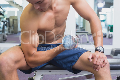 Fit man lifting dumbbells sitting on the bench