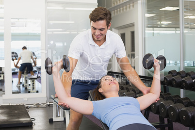 Personal trainer helping client lift dumbbells