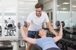 Personal trainer helping client lift dumbbells