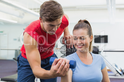 Personal trainer helping client lift dumbbell