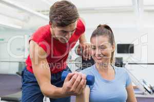 Personal trainer helping client lift dumbbell