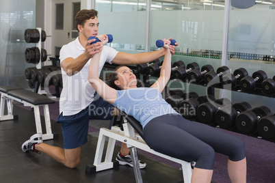 Personal trainer helping client lift dumbbells