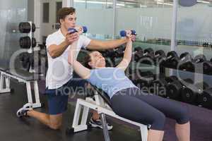 Personal trainer helping client lift dumbbells