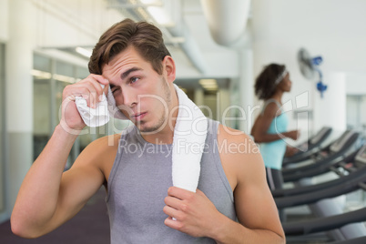 Handsome man wiping his forehead beside treadmills