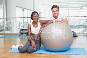 Personal trainer and client smiling at camera with exercise ball