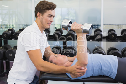 Personal trainer helping client lift dumbbells