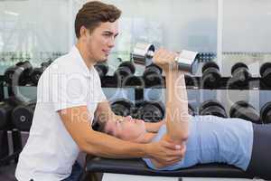 Personal trainer helping client lift dumbbells