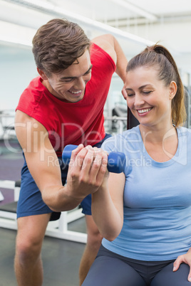 Personal trainer helping client lift dumbbell