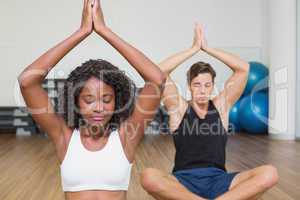 Fit couple sitting in lotus pose in fitness studio