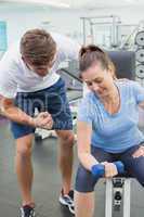 Personal trainer helping client lift dumbbell