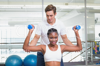 Personal trainer helping client lift dumbbells on exercise ball