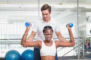 Personal trainer helping client lift dumbbells on exercise ball