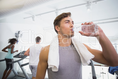 Fit man drinking water beside treadmills