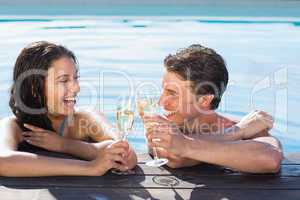 Cheerful couple toasting champagne in swimming pool