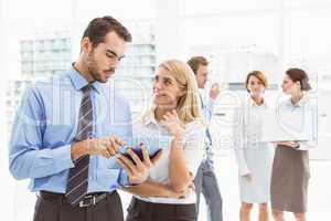 Business couple using digital tablet with colleagues behind