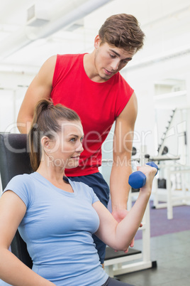 Personal trainer helping client lift dumbbell