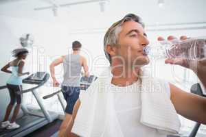 Fit man drinking water beside treadmills
