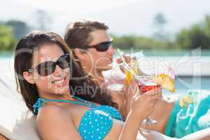 Young couple with drinks by swimming pool