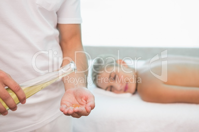 Masseur holding oil with woman lying background at spa center