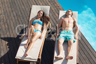 Couple resting on sun loungers by swimming pool
