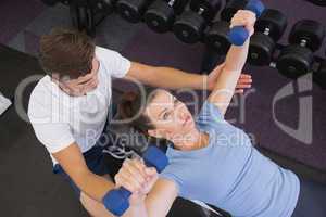 Personal trainer helping client lift dumbbells