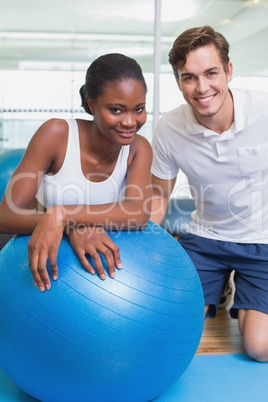 Personal trainer and client smiling at camera with exercise ball