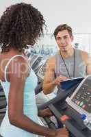 Fit woman on treadmill talking to personal trainer