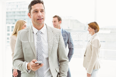 Businessman text messaging with colleagues in meeting behind Businessman text messaging with colleagues in meeting behind