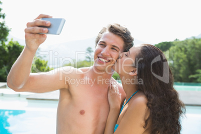 Couple taking picture of themselves by swimming pool on a sunny
