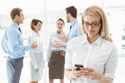 Businesswoman text messaging with colleagues in meeting behind