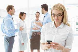 Businesswoman text messaging with colleagues in meeting behind