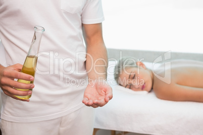 Masseur holding oil with woman lying background at spa center