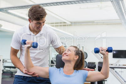 Personal trainer helping client lift dumbbell