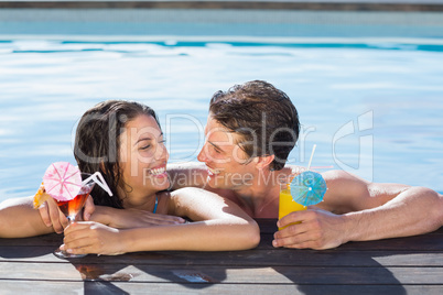 Cheerful couple with drinks in swimming pool