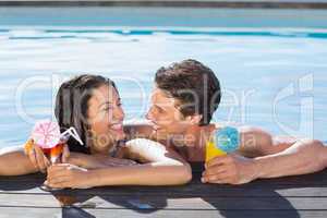 Cheerful couple with drinks in swimming pool