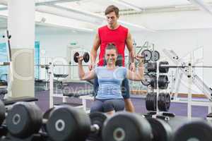 Personal trainer helping client lift dumbbells