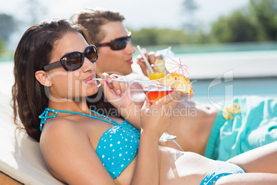 Young couple with drinks by swimming pool