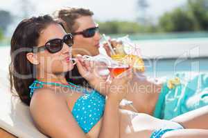Young couple with drinks by swimming pool