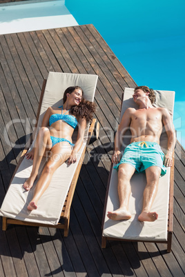 Couple resting on sun loungers by swimming pool