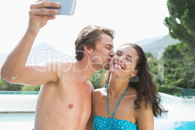 Couple taking picture of themselves by swimming pool on a sunny