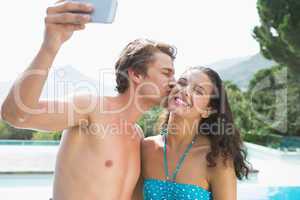 Couple taking picture of themselves by swimming pool on a sunny