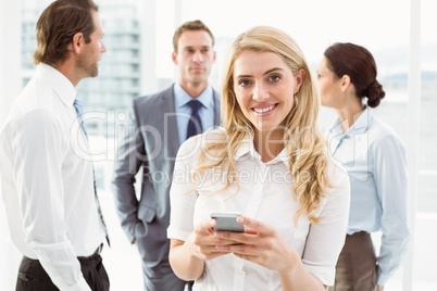 Businesswoman text messaging with colleagues in meeting behind Businesswoman text messaging with colleagues in meeting behind
