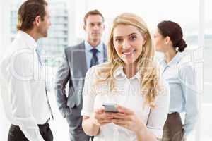 Businesswoman text messaging with colleagues in meeting behind