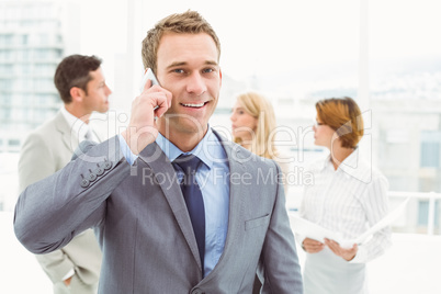 Businessman using mobile phone with colleagues behind