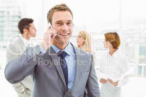 Businessman using mobile phone with colleagues behind